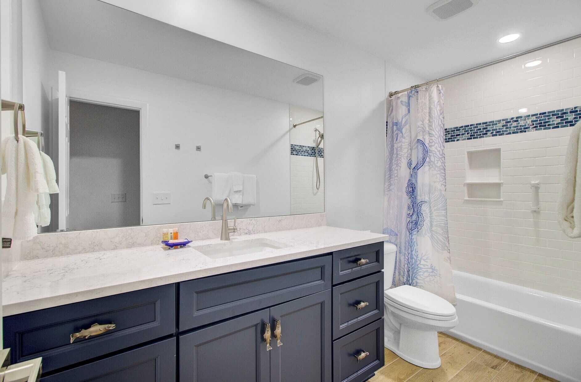 A modern bathroom with a white sink, dark blue cabinets, a large mirror, and a shower with a blue and white tile border.