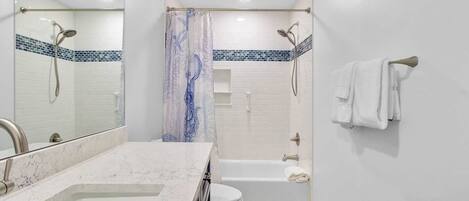 Un baño con lavamanos blanco, espejo, inodoro, bañera y ducha.