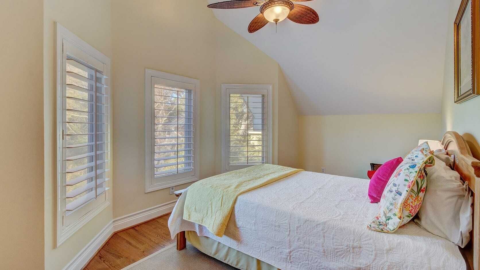 A bedroom with a bed, a ceiling fan, and three windows.