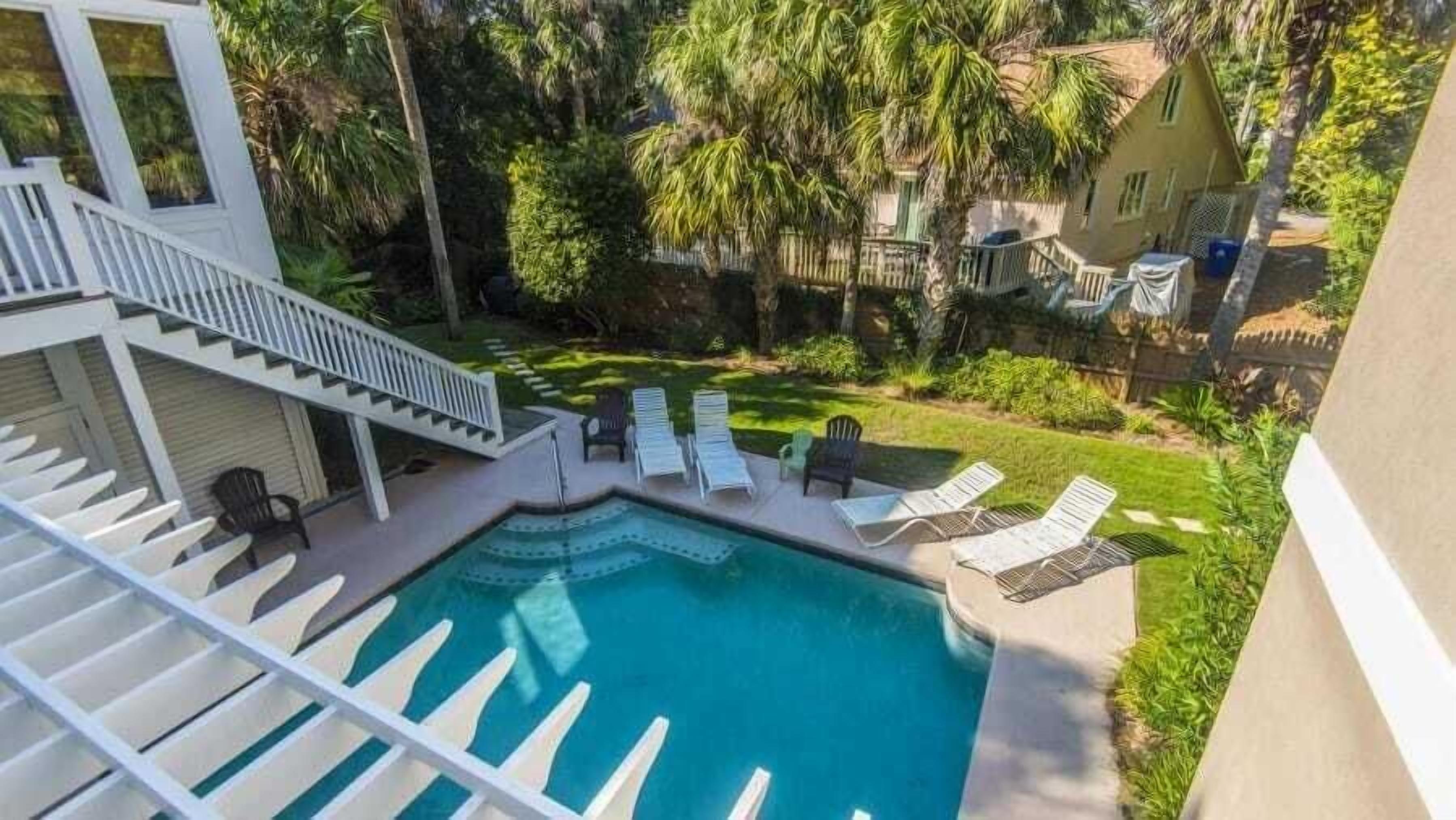 A swimming pool with lounge chairs, a staircase, and a well-maintained lawn.