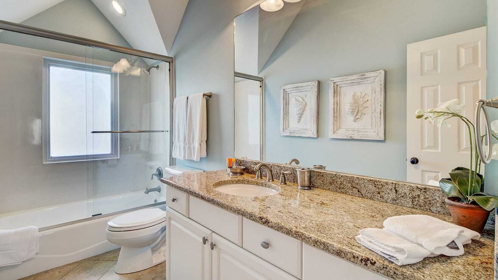 Un baño moderno con lavamanos de granito, ducha con cerramiento de vidrio y un inodoro blanco.