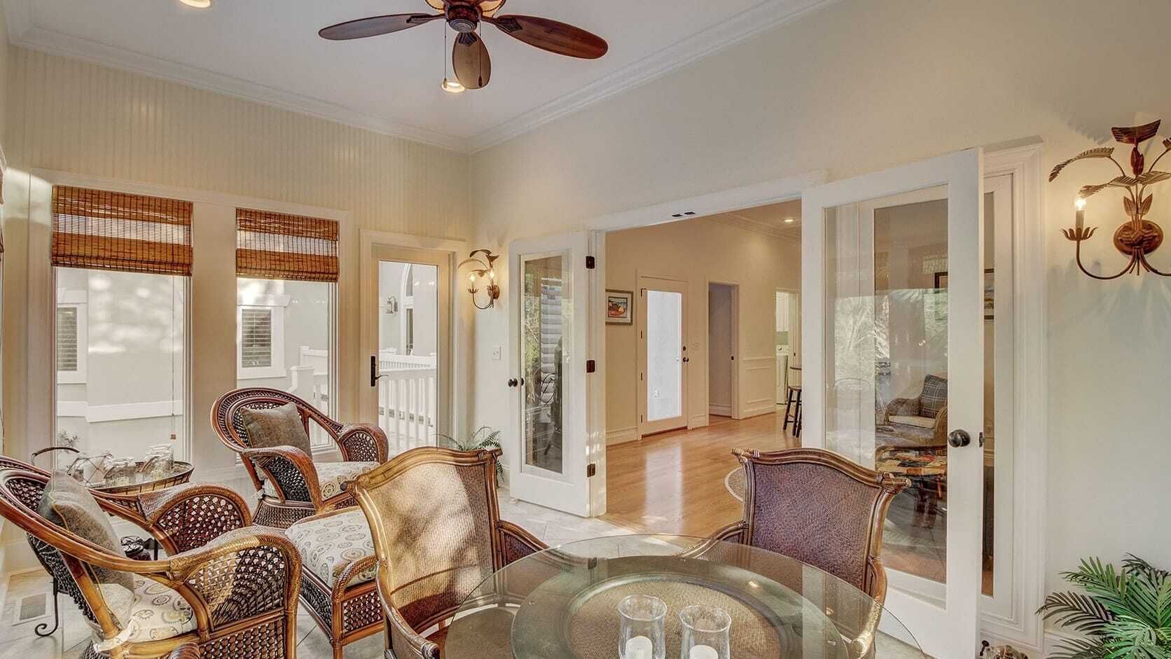 A spacious room with a glass dining table, wicker chairs, and a ceiling fan.