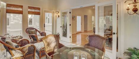 A spacious room with a glass dining table, wicker chairs, and a ceiling fan.