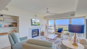 A spacious living room with a fireplace, comfortable seating, a television, and a view of the ocean.