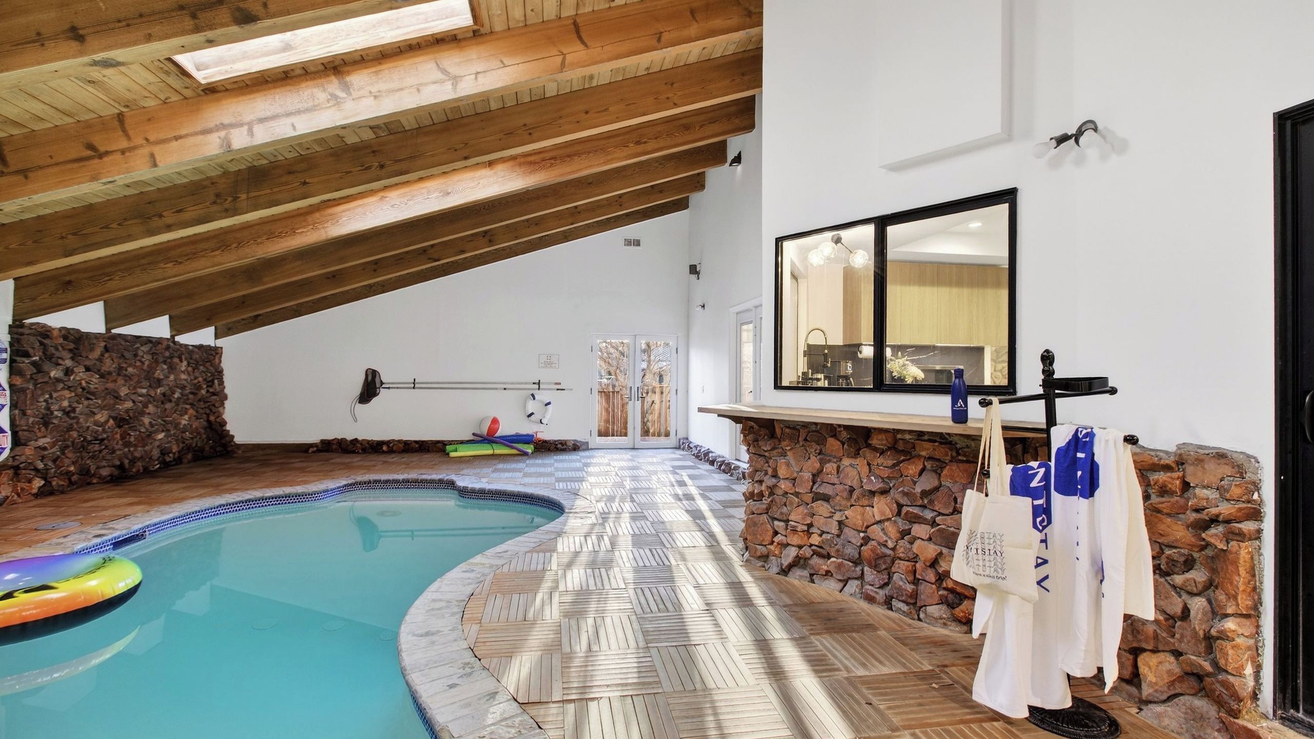 Une piscine intérieure avec un plafond en bois, un mur en pierre et un sol carrelé.