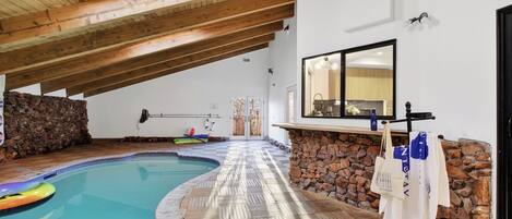 Une piscine intérieure avec un plafond en bois, un mur en pierre et un sol carrelé.