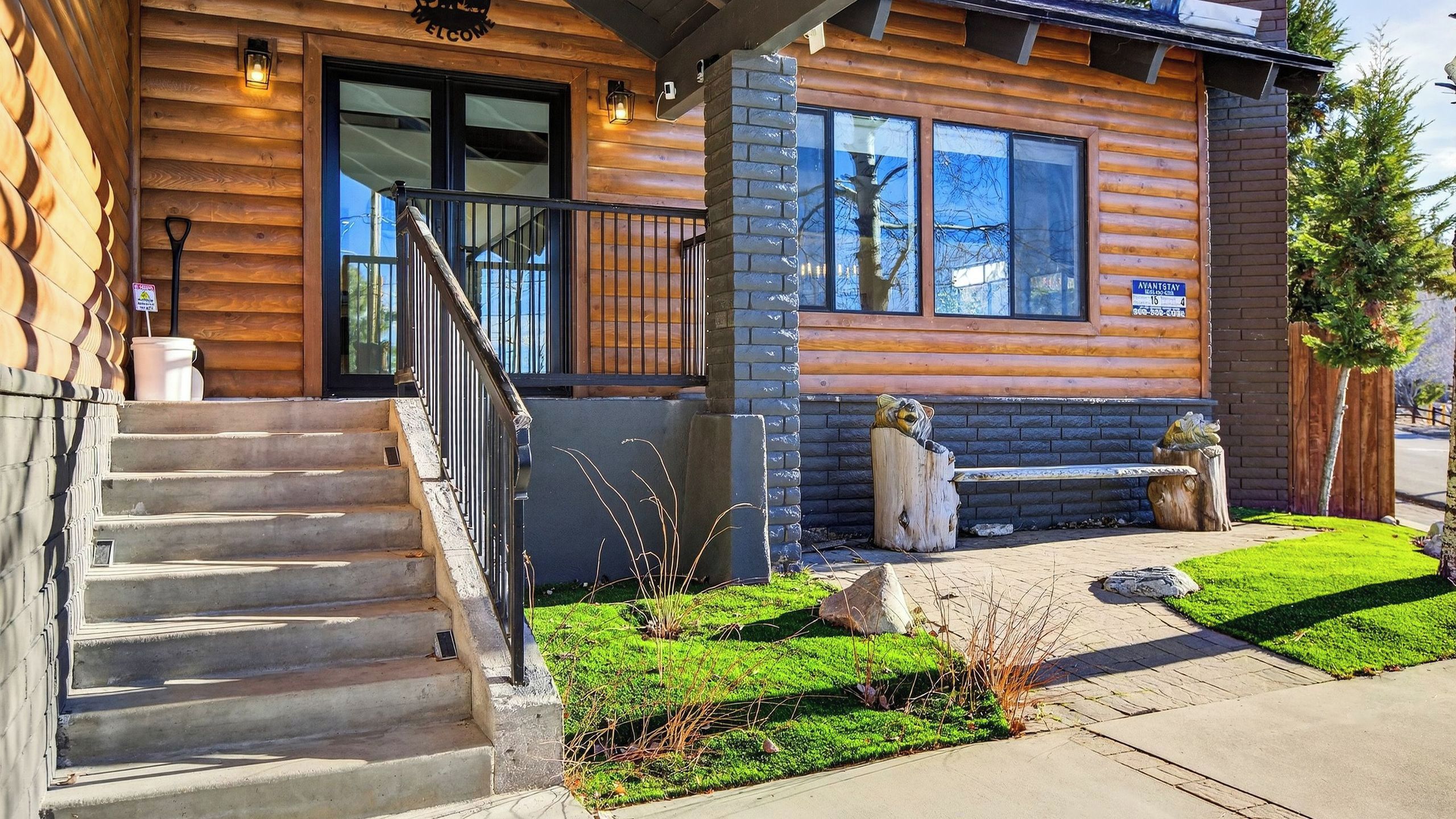 A log cabin-style building with a wooden exterior, a front porch, a staircase, and a well-maintained lawn.