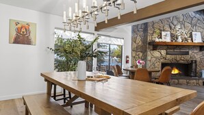 A dining area with a wooden table, chairs, a fireplace, and a stone wall.