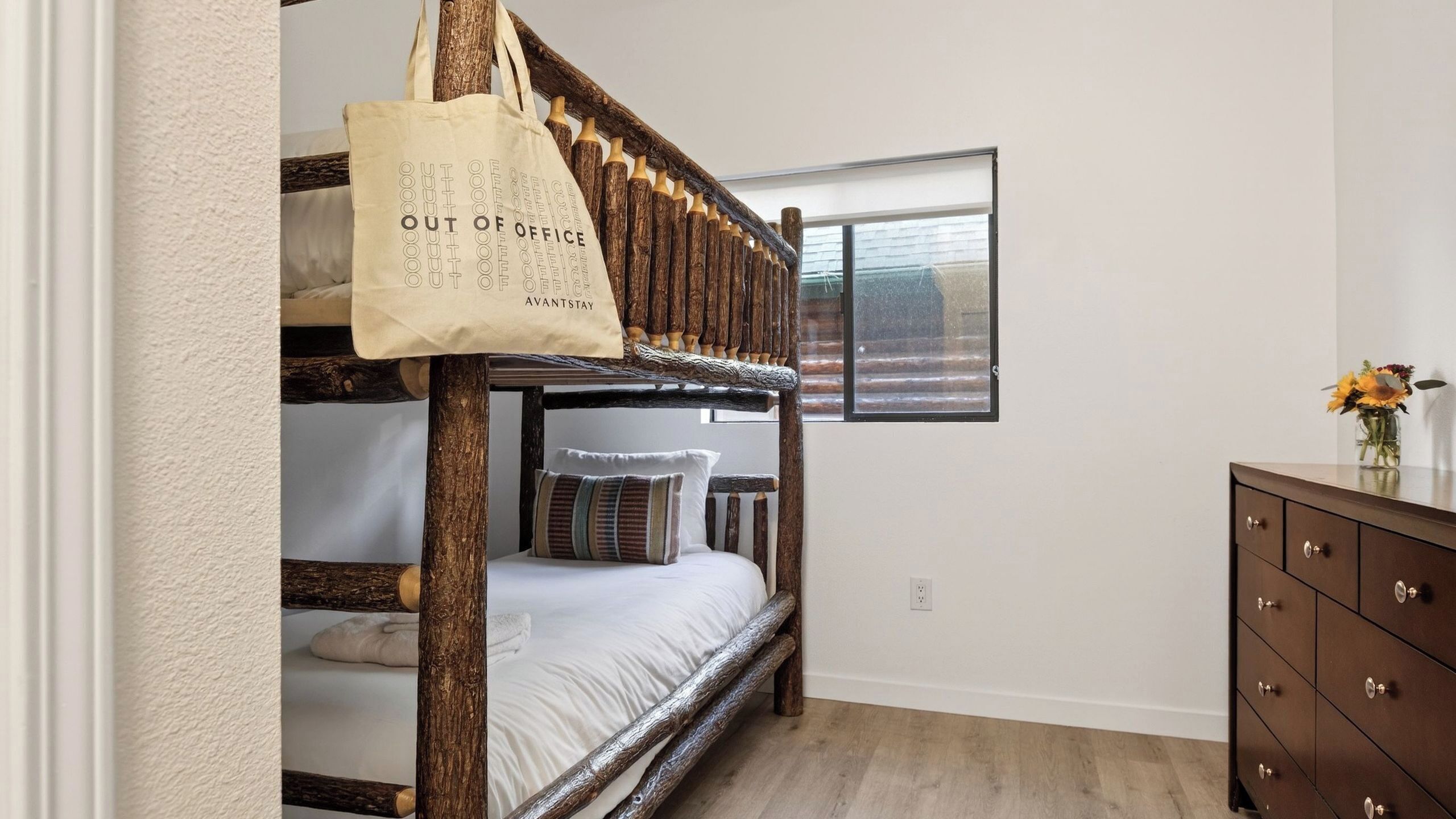 Een stapelbed met een houten frame, een wit kussen en een beige opbergtas bungelend aan de zijkant.
