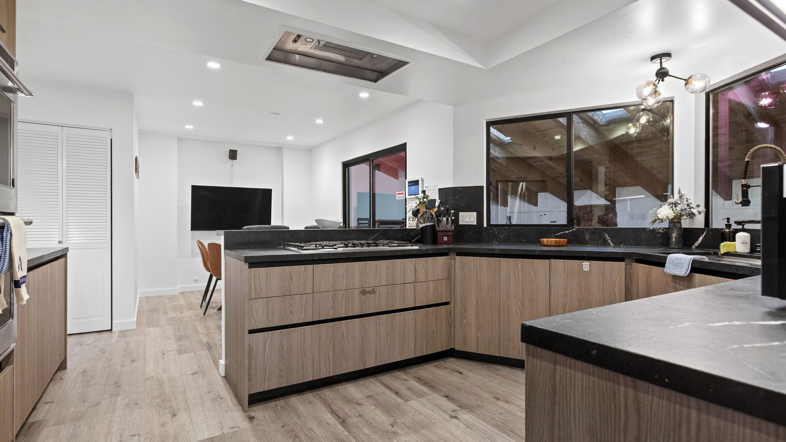 A modern kitchen with a large island, built-in appliances, and a large window providing natural light.