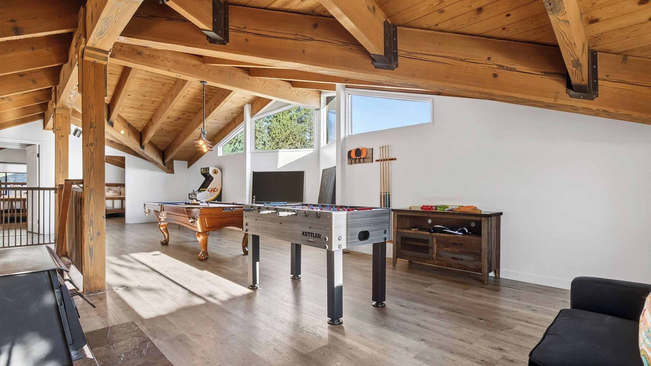 Een ruime loft met houten balken, een tafelvoetbaltafel, een pooltafel en een biljarttafel.