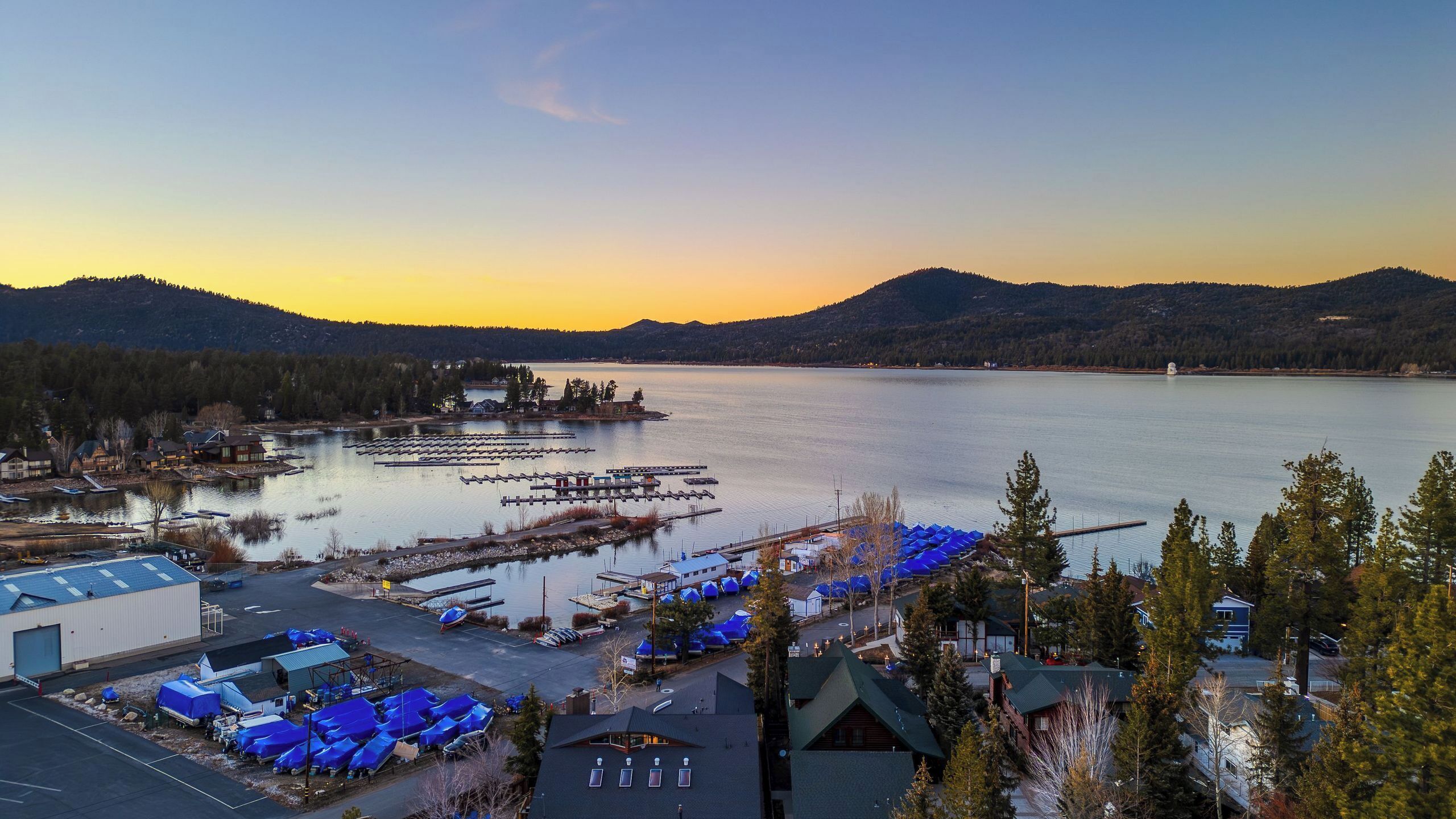 A lakeside property with docked boats, a marina, and a parking area with blue canopies.