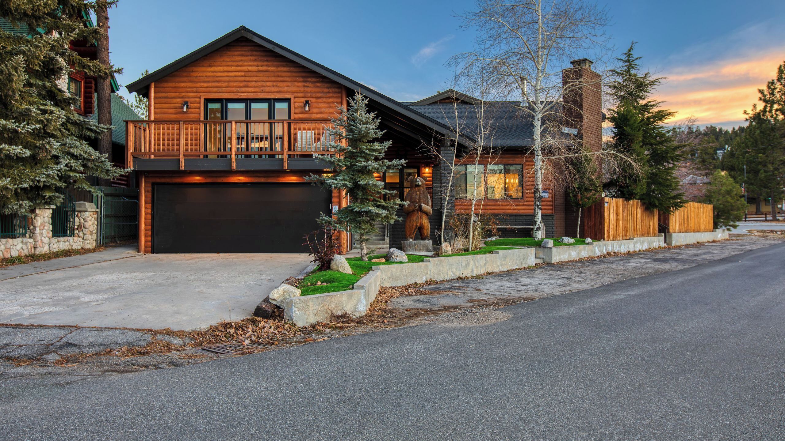 A log cabin with a balcony, a garage, and a stone wall.