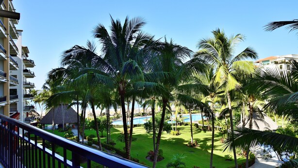 A resort with a pool, palm trees, and a thatched-roof structure.