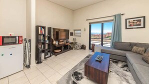 Una sala de estar con un sofá, una mesa de centro, un televisor, una estantería y un ventanal con vistas.