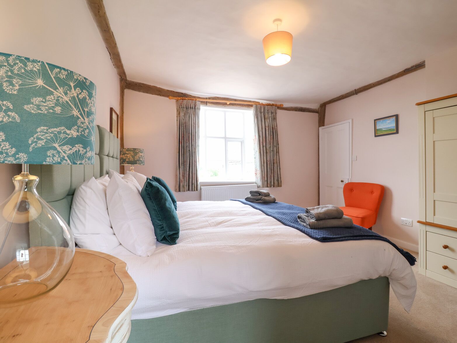 A bedroom with a bed, a chair, a lamp, and a window with curtains.