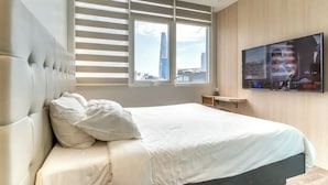 Una habitación de hotel moderna con una cama grande, un televisor montado en la pared y una ventana con persianas.