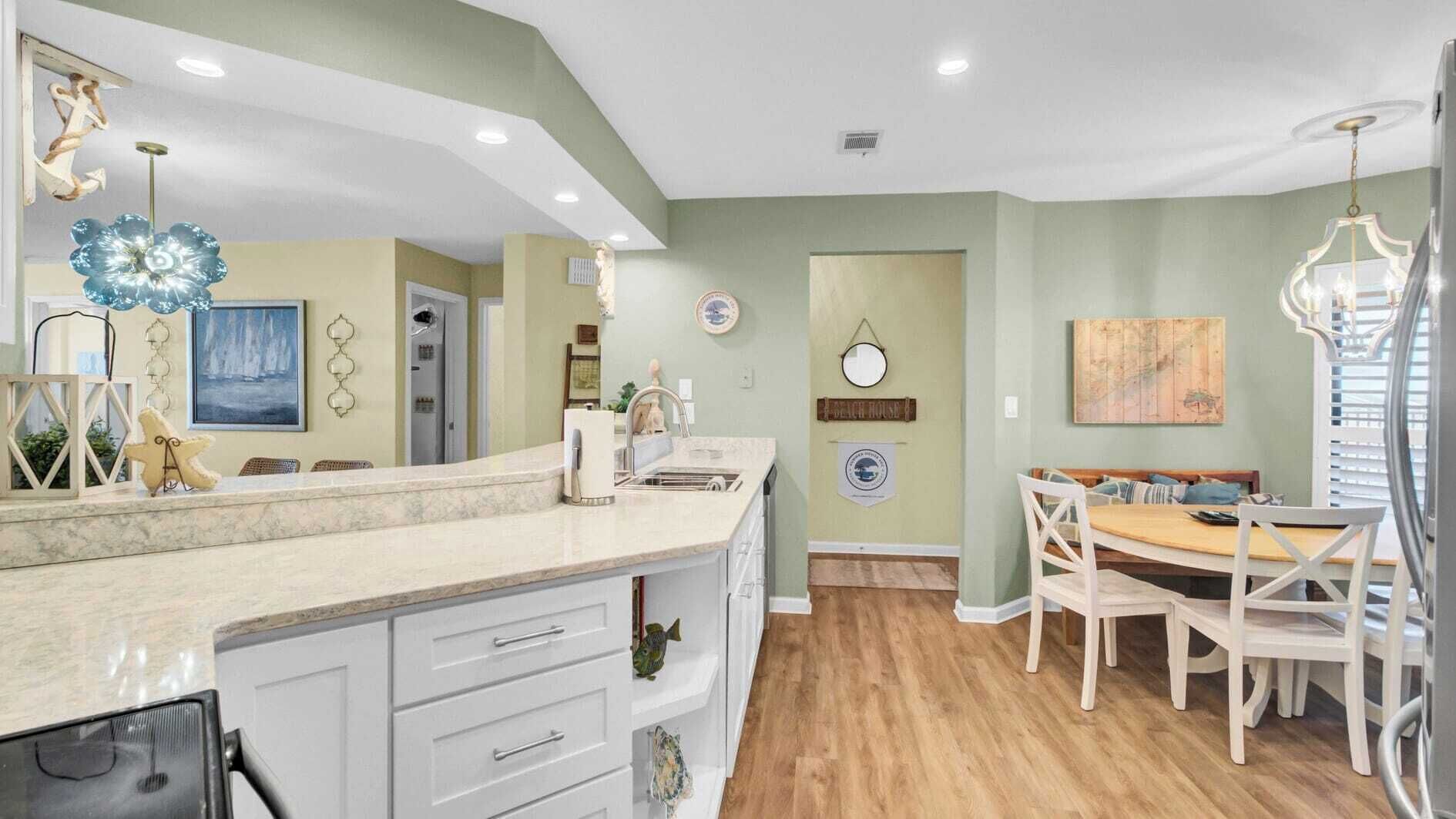 A kitchen with a marble countertop, white cabinets, and a dining area with a wooden table and white chairs.