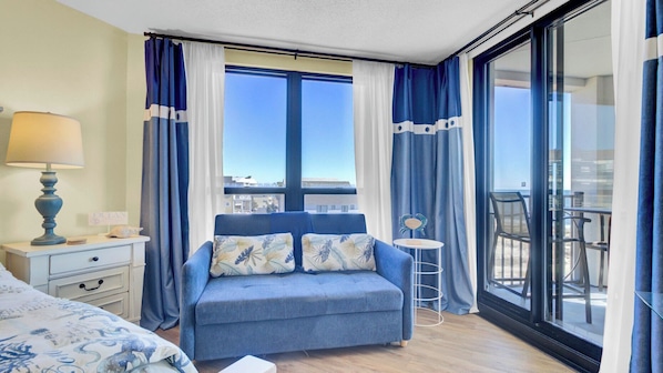 Une chambre d’hôtel avec un lit, une table de chevet, une lampe, une petite table avec une chaise, et un balcon avec vue.