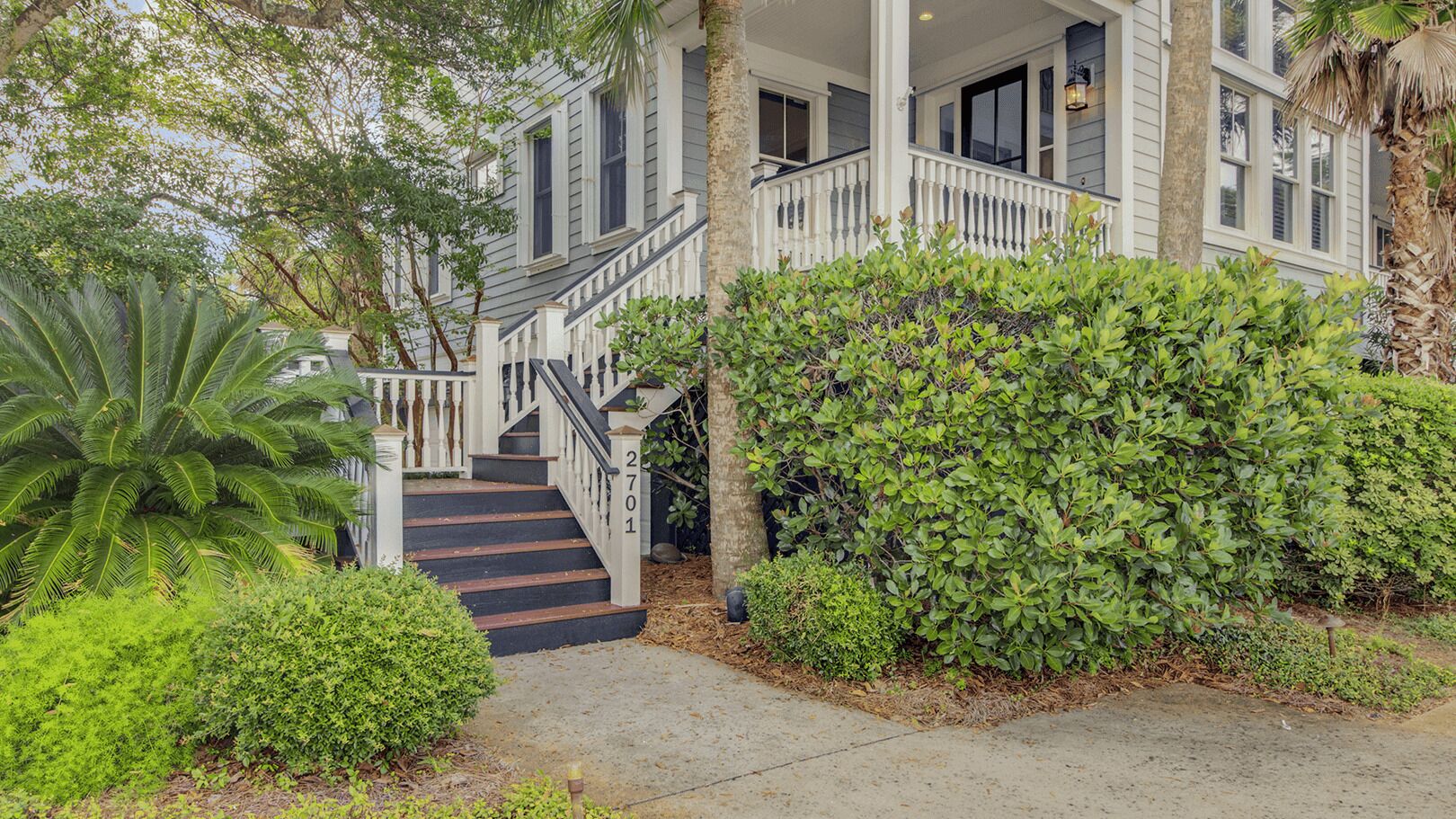A two-story house with a white exterior, a black staircase, and a well-maintained garden with various plants and a palm tree.
