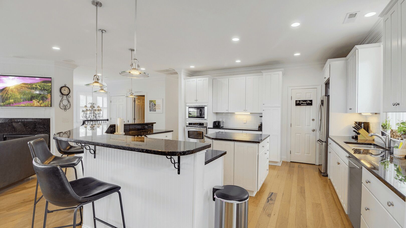 Una cocina moderna con armarios blancos, una isla central con taburetes de bar, electrodomésticos de acero inoxidable e iluminación colgante.