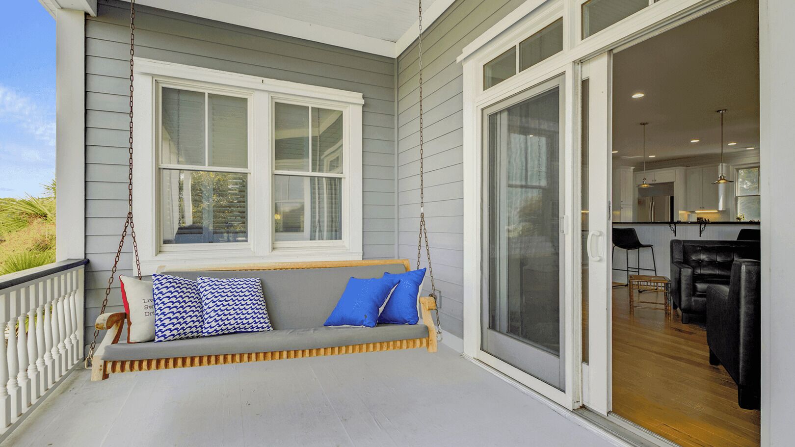 A porch with a swing, a sliding glass door leading to a kitchen, and a view of the outdoors.