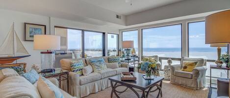 A spacious living room with a large window overlooking the ocean, a ceiling fan, and a cozy seating area with a coffee table.