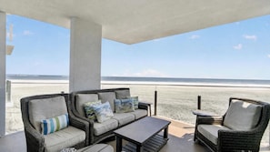 A balcony with wicker furniture, a view of the beach, and a clear sky.