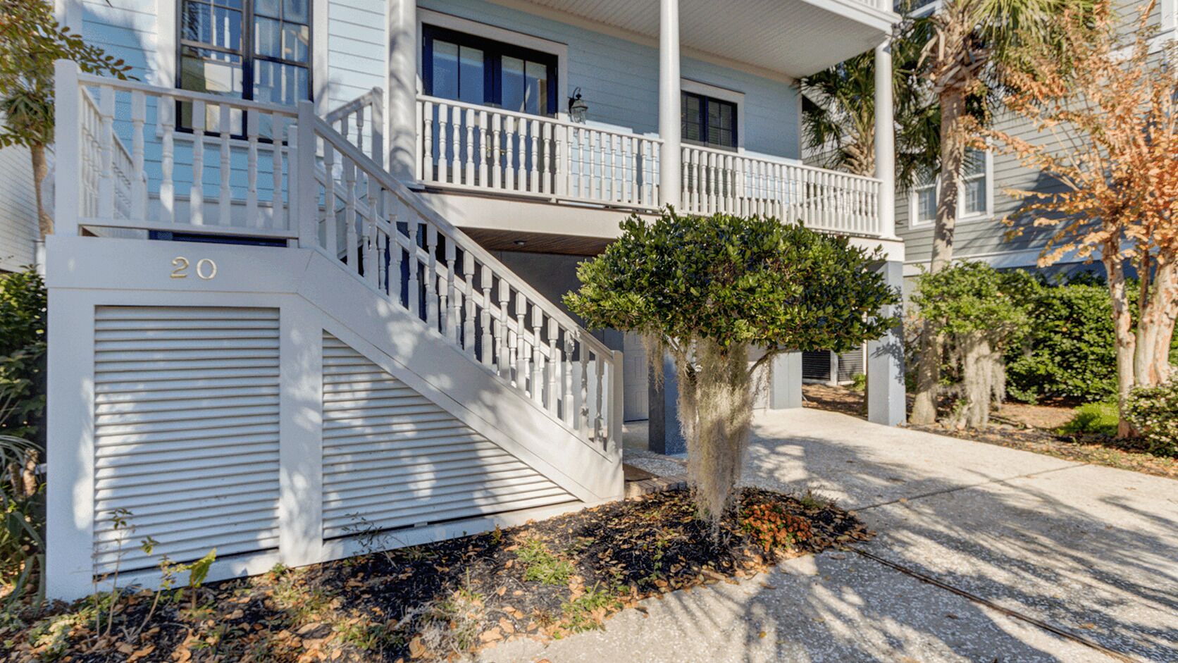 A two-story building with a white exterior, a balcony on the upper floor, and a small tree in front.