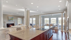A spacious kitchen with a large island, white cabinetry, and a fireplace.