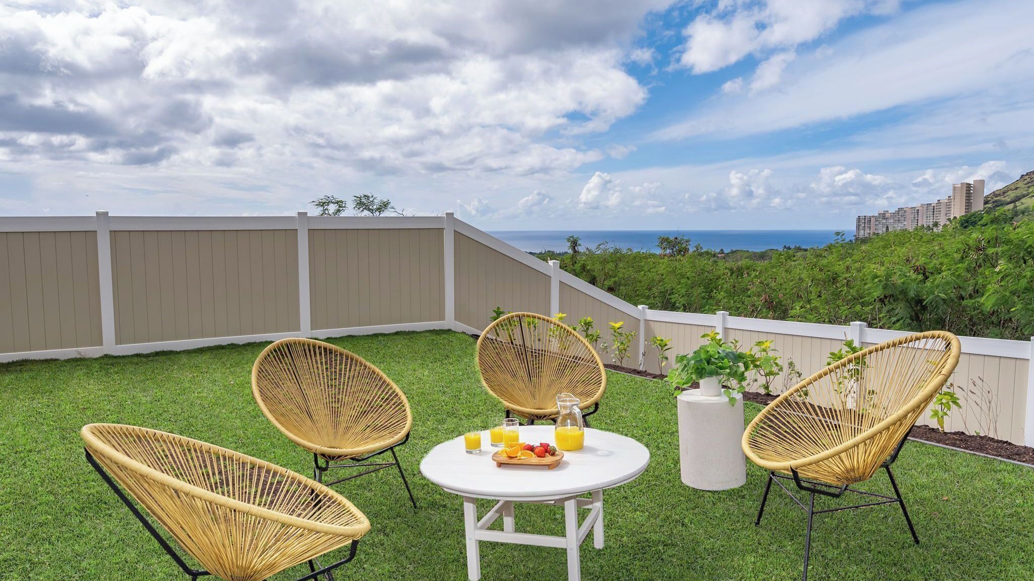 A patio with four wicker chairs, a white table, and a fruit basket with drinks.