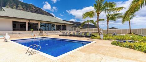 A swimming pool with a clear blue water, surrounded by lounge chairs and palm trees, with a building in the background.