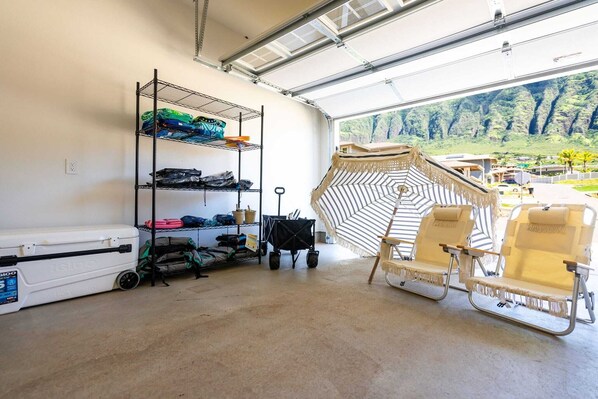 A garage with a large window, a metal shelving unit, a white cooler, and two beach chairs. - Alaula by Avantstay Gated Security Home w Valley, Ocean Views! (Waianae)