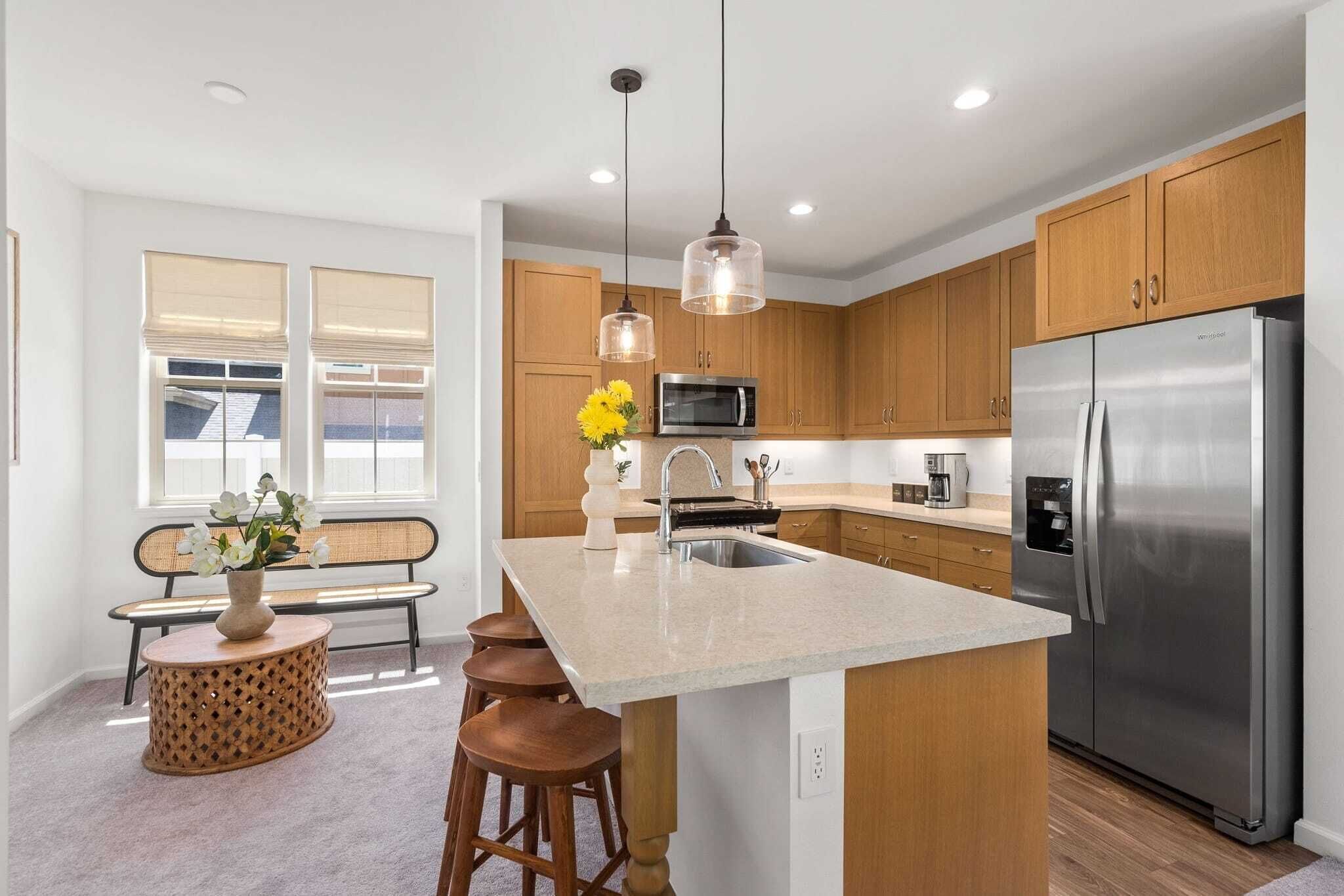 Una cocina moderna con gabinetes de madera, electrodomésticos de acero inoxidable, una isla central con taburetes e iluminación colgante.