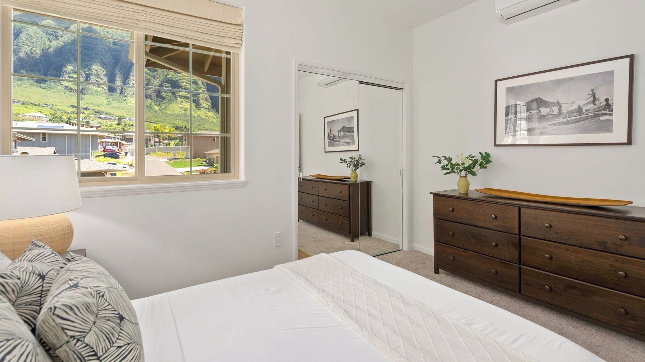A bedroom with a bed, a dresser, a window with a view of a green landscape, and a framed picture on the wall.