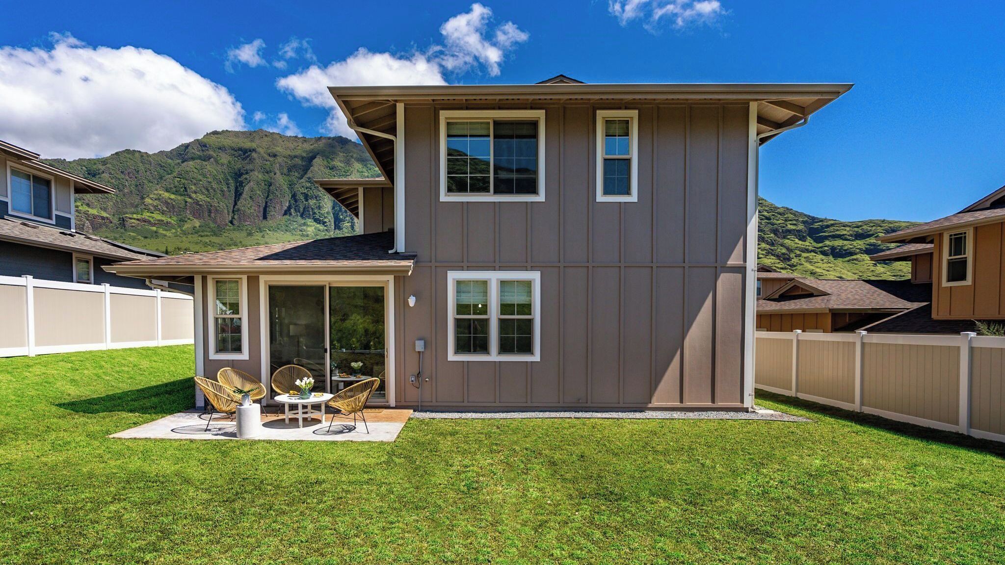 A two-story house with a covered patio, a fenced backyard, and a mountainous backdrop.