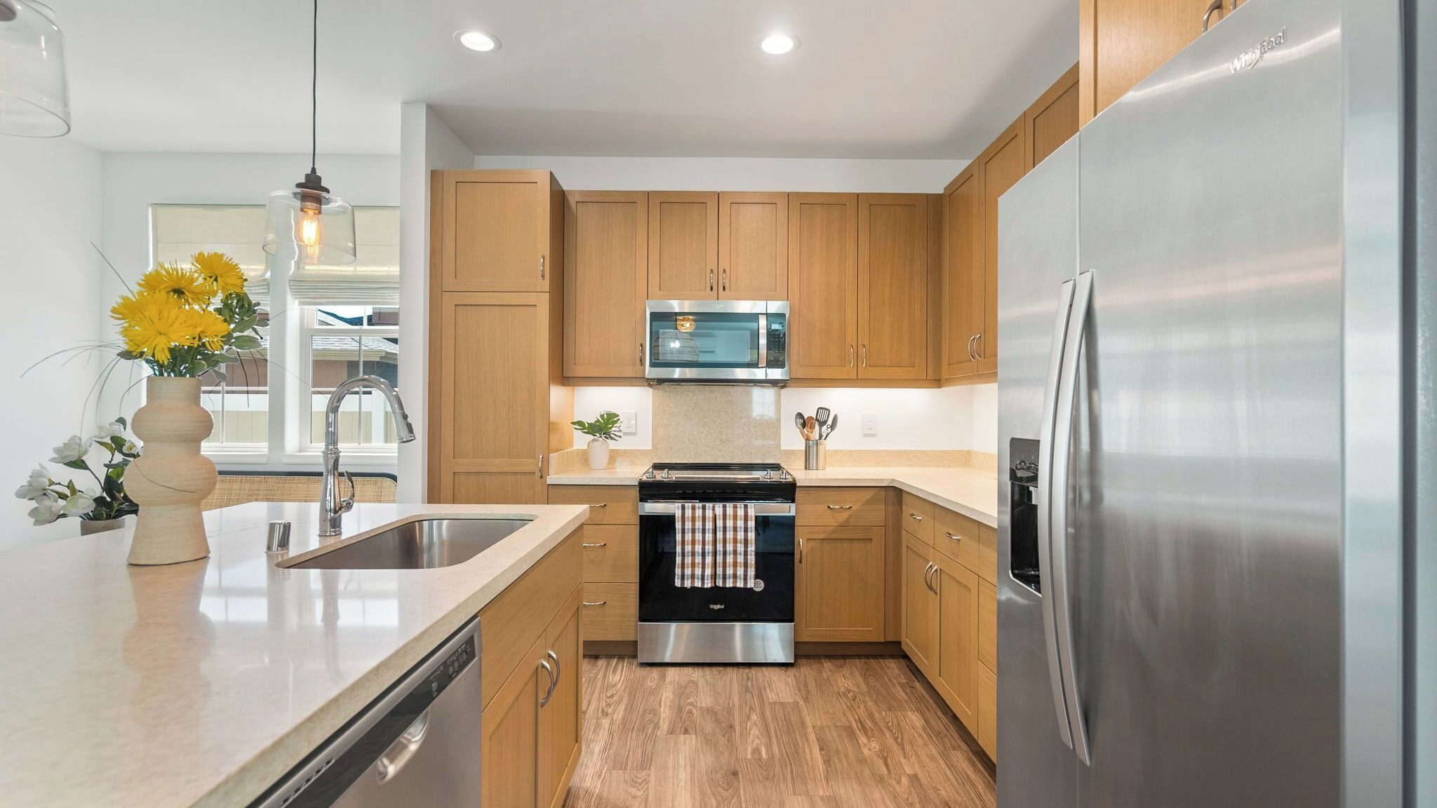 A modern kitchen with wooden cabinets, stainless steel appliances, and a central island with a sink and a vase of flowers.