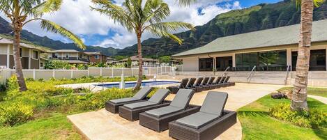 A pool area with lounge chairs, palm trees, and a building with a tiled roof.
