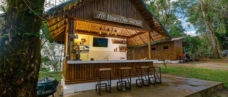 A rustic wooden structure labeled "He Brews Cafe and Bar" with a bar area and seating.