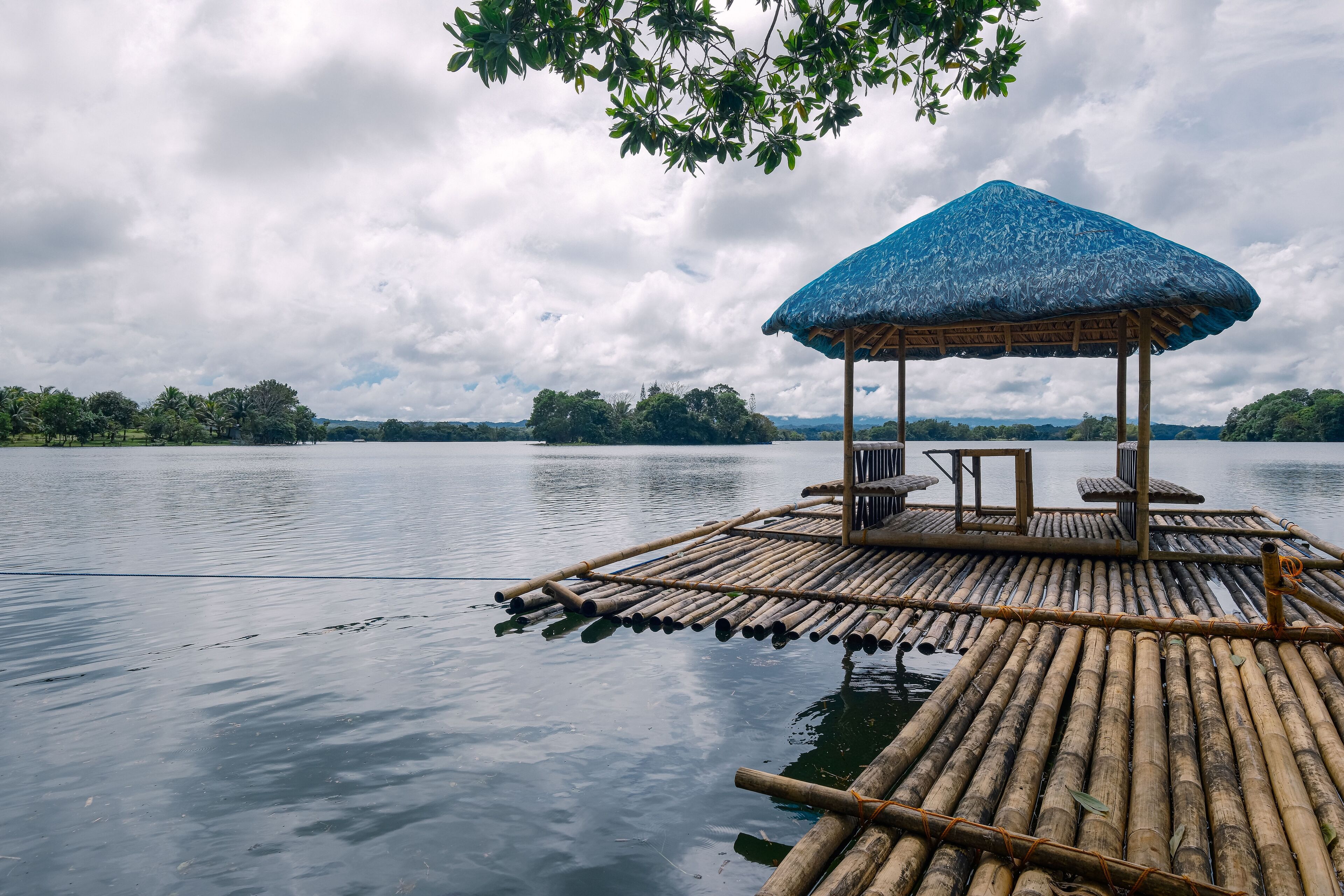 A bamboo raft with a thatched roof and seating, floating on calm water.