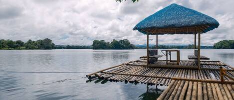A bamboo raft with a thatched roof and seating, floating on calm water.