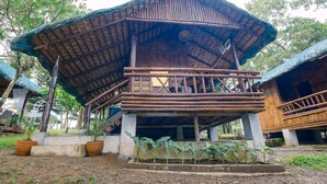 Una estructura de madera con techo de paja, un balcón y base de concreto.