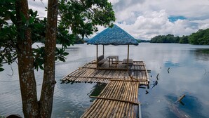 Una balsa de bambú con techo de paja y zona de estar, flotando sobre aguas tranquilas.
