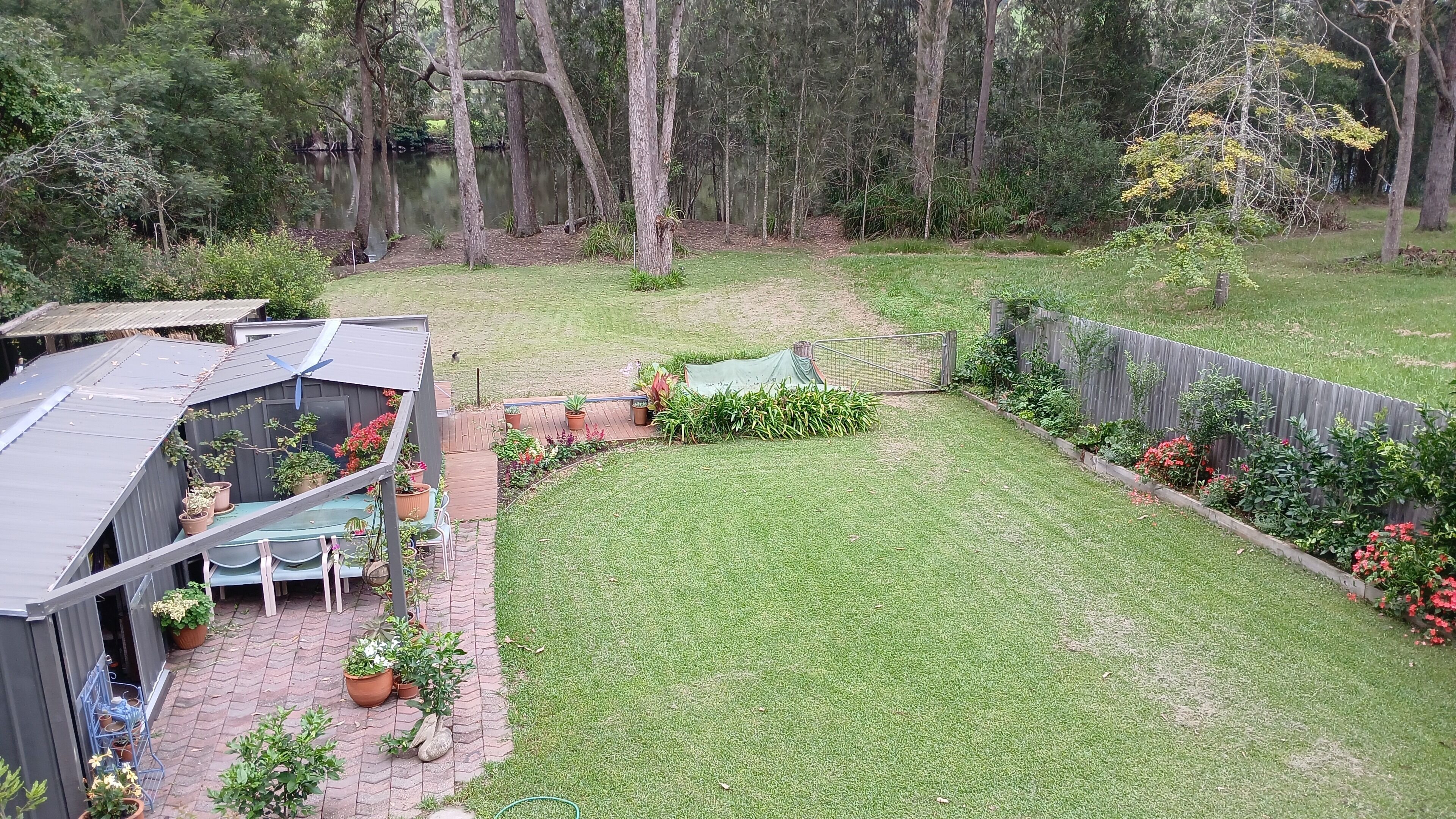 Un jardin avec une zone délimitée par une clôture, un petit abri de jardin et une pelouse.