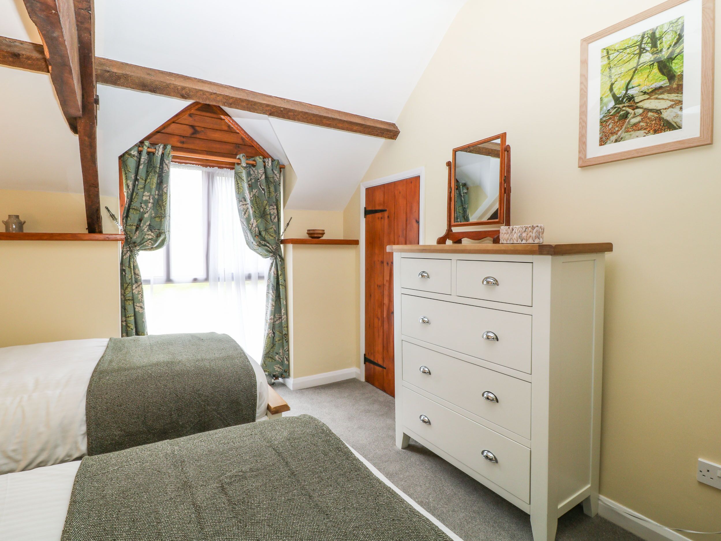 A bedroom with a bed, a dresser, a mirror, and a window with curtains.