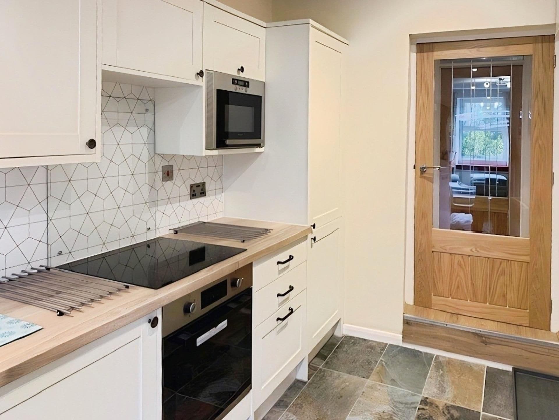 A modern kitchen with a built-in stove, microwave, and oven. There are white cabinets and a tiled backsplash. A wooden door is visible to the right.