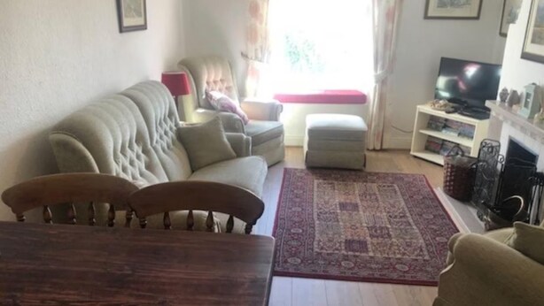 A living room with a sofa, ottoman, wooden table, and a TV on a stand.