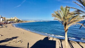 A beach with a palm tree, clear blue sky, and buildings in the background. - Modern apartment close to the beach (Benalmádena)