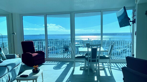 Ein geräumiger Balkon mit freiem Blick auf das Meer und die Stadt, ausgestattet mit einem roten Sessel, einem weißen Tisch und Stühlen.