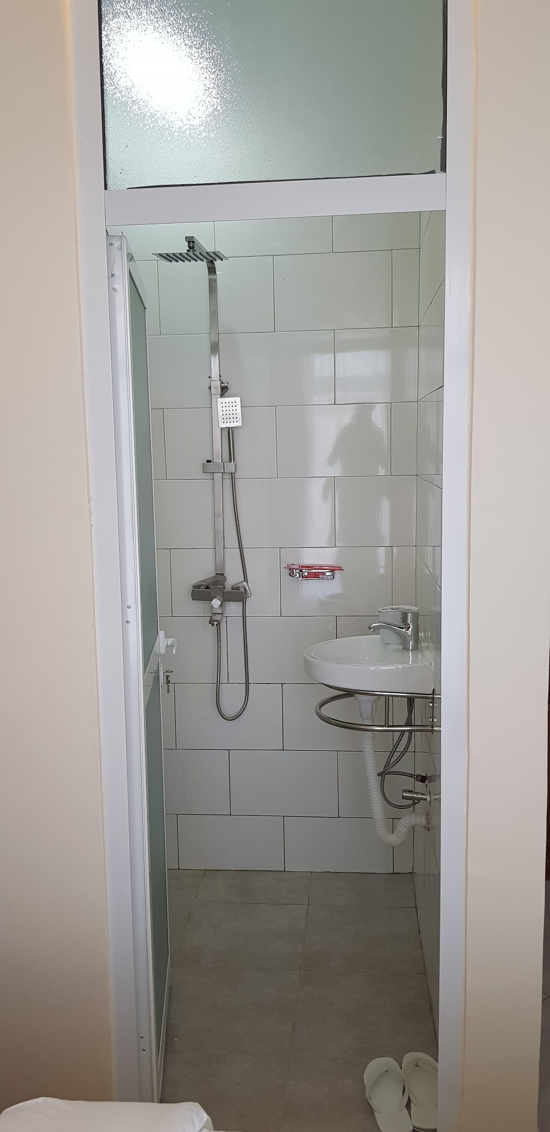 A small, enclosed bathroom with a shower, a sink, and a toilet.